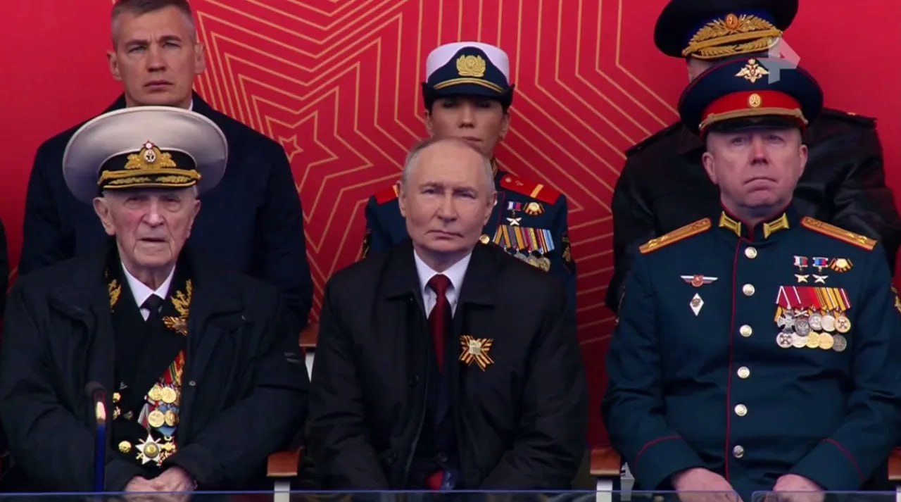 Рядом с Владимиром Путиным на трибуне сидят ветеран Великой Отечественной войны Свет Турунов и герой РФ Леонид Рыжов